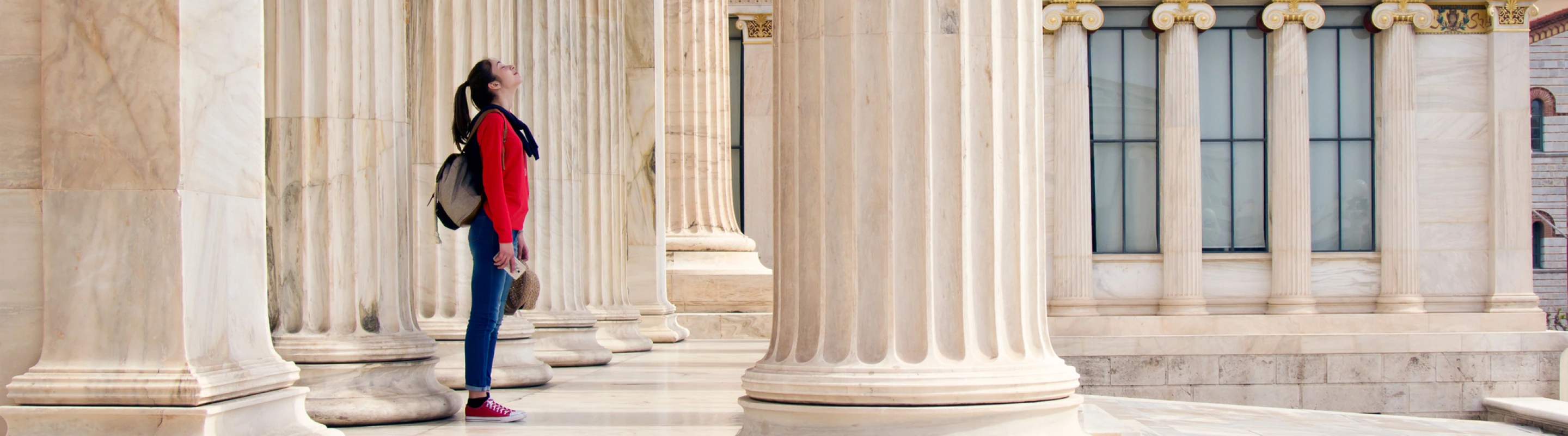 a young woman with cancel for any reason travel insurance awes at classical architecture as she stands between marble columns 