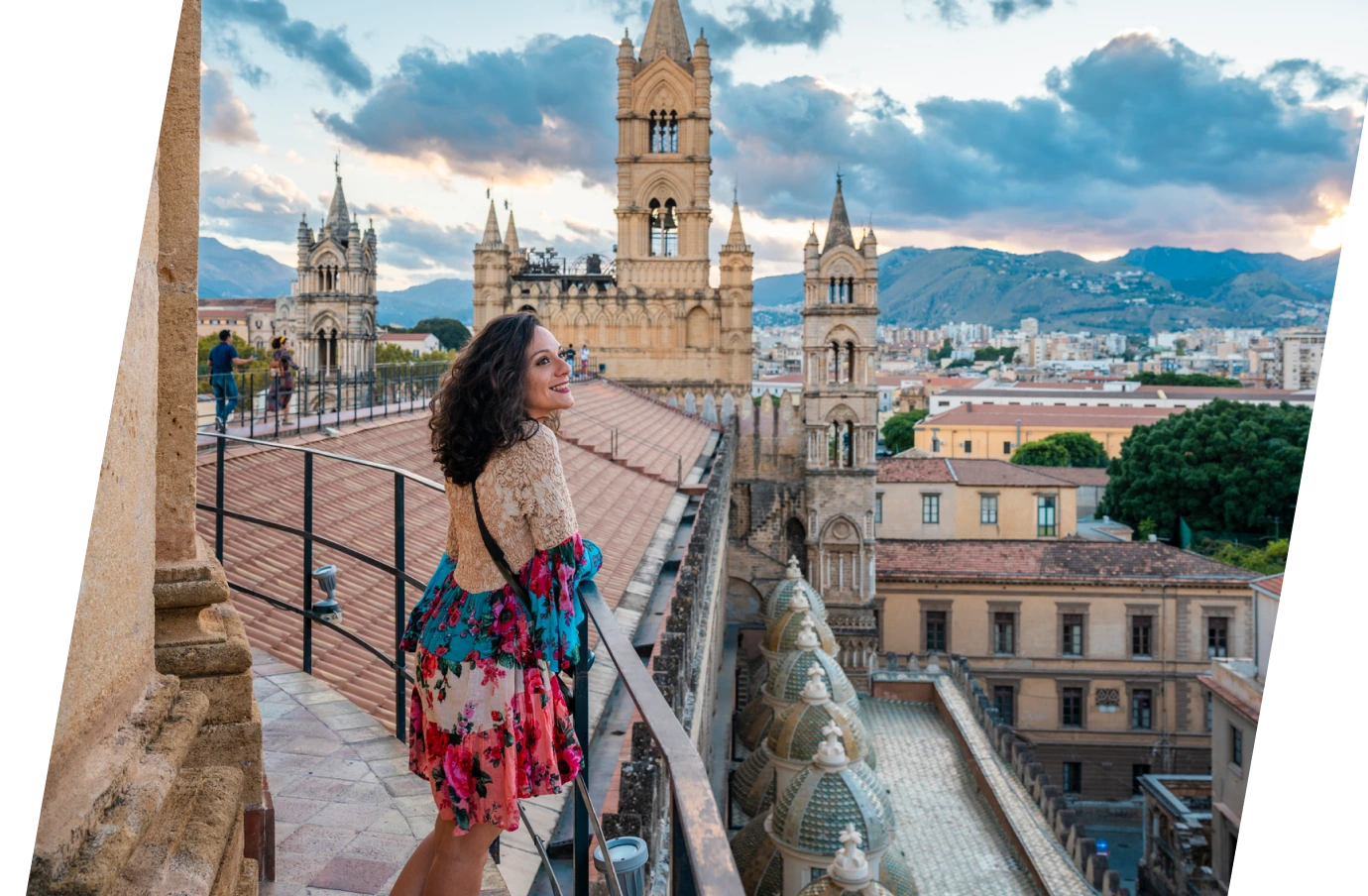 a middle-aged woman with international travel insurance stands on a rooftop terrace to take in views of Palermo, Italy
