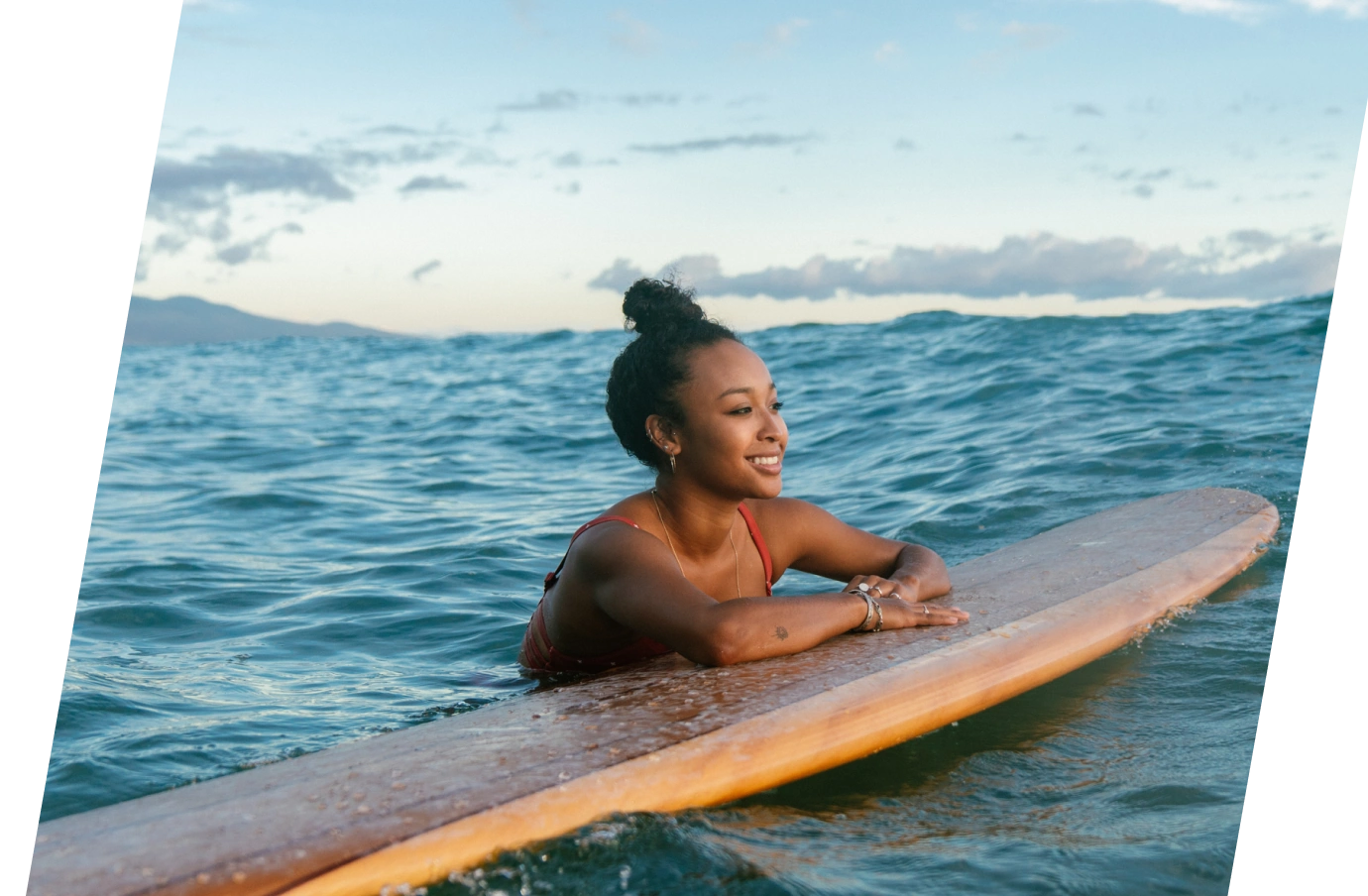 young woman with affordable travel insurance in the ocean with her arms on a surfboard