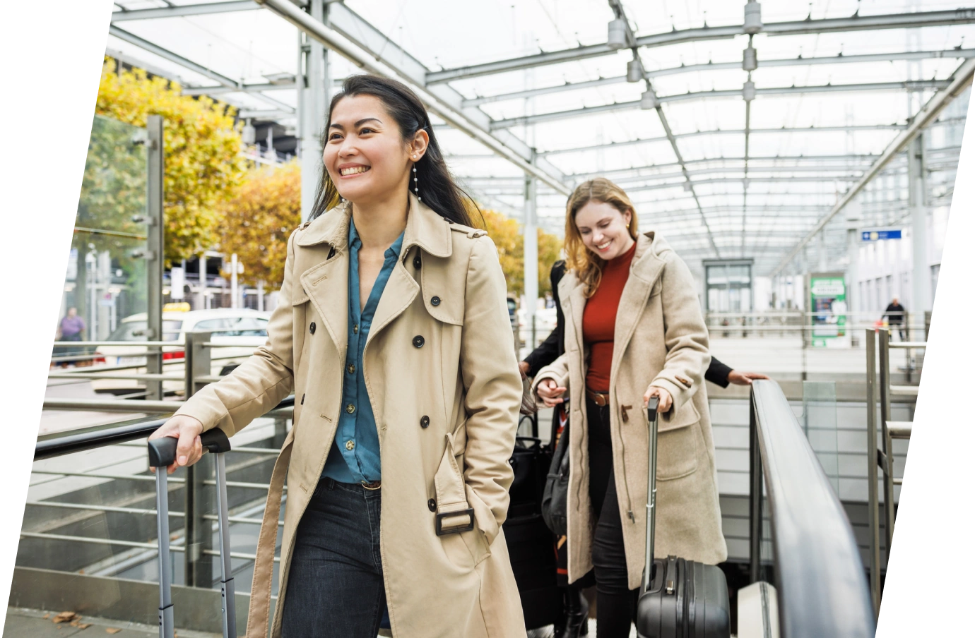 two, young women in professional attire roll their suitcases outdoors, insured with business travel insurance 