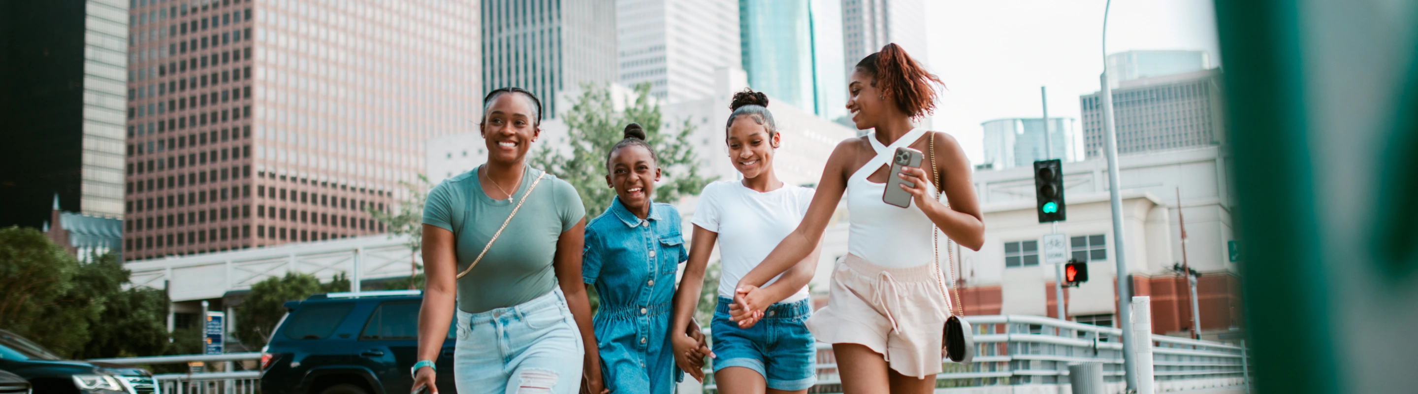 two older sisters hold their younger sisters' hand as they cross a street in Houston, insured with travel insurance for Texas