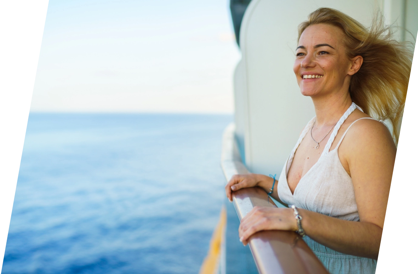 a young, blonde woman in a flowy, white dress stands on a ship's balcony over the ocean, insured with cruise travel insurance