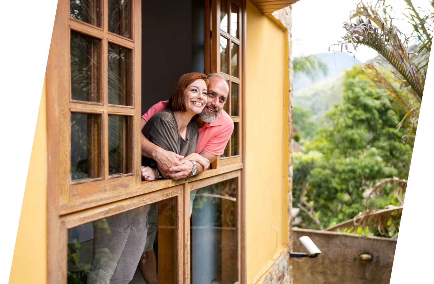 Couple with vacation rental travel insurance embracing and leaning out a window to look at the view