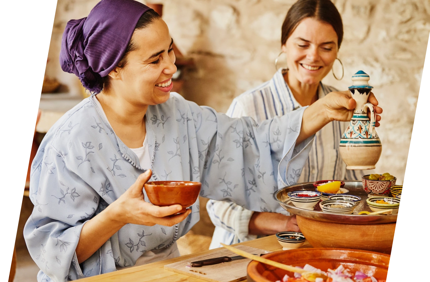 Two women with travel insurance for cultural trips share food in small bowls in a rustic setting 
