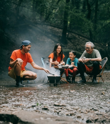 a multi-generational family with travel insurance for nature trips sits and cooks by the fire in the shallow water of a creek