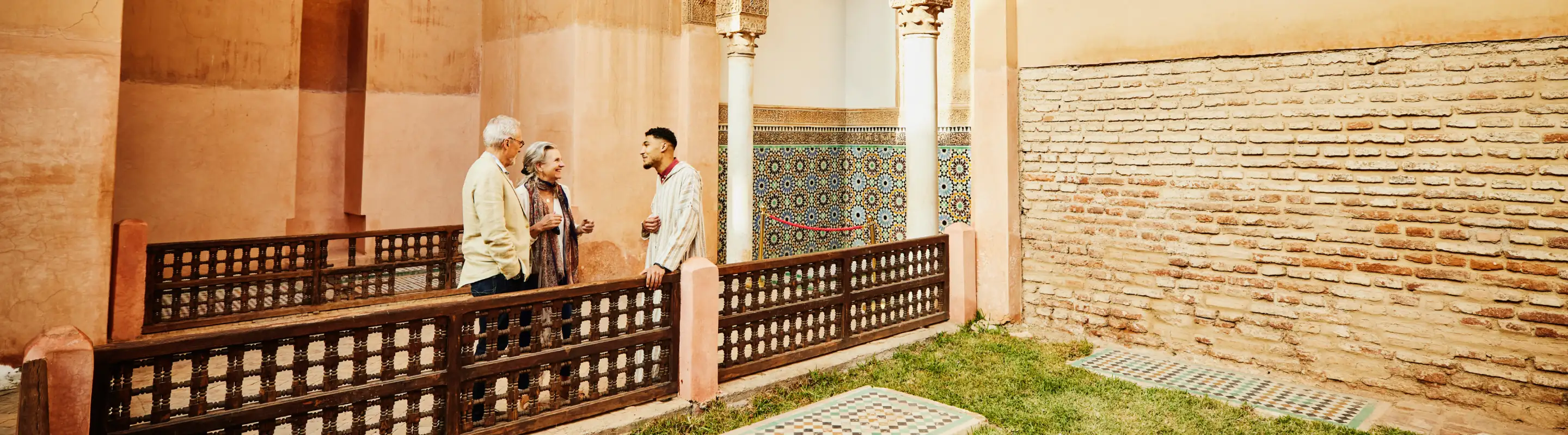 an older couple with travel insurance for cultural trips talks to their guide in an architectural courtyard with tiles