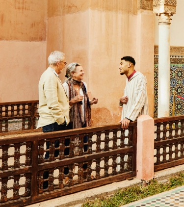 an older couple with travel insurance for cultural trips talks to their guide in an architectural courtyard with tiles