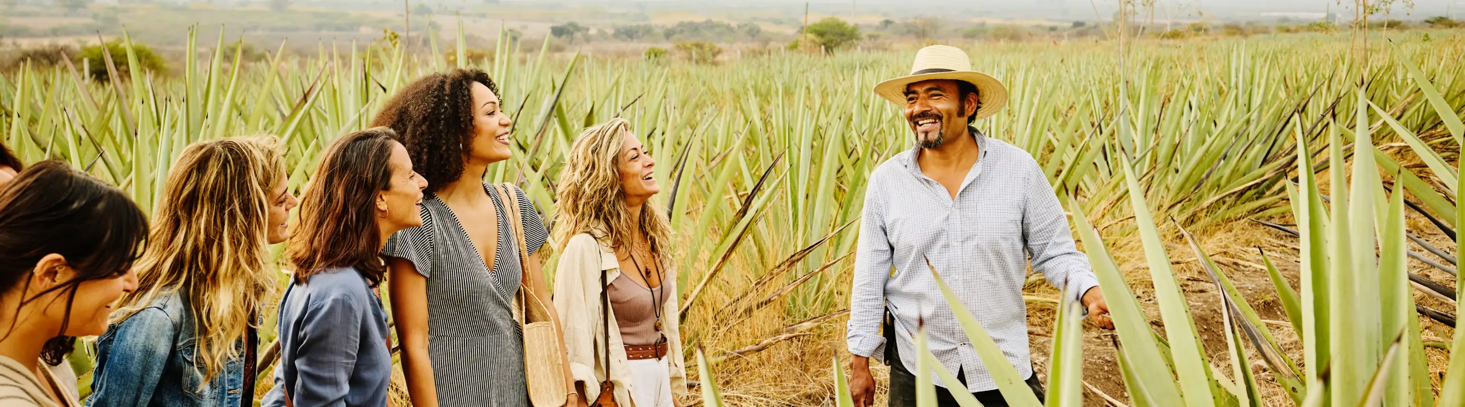 a young tour group with travel insurance for cultural trips stands among agave plants with a local guide