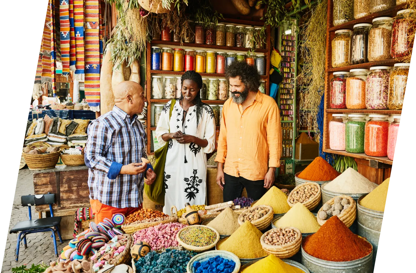 two Black travelers with travel insurance for culinary vacations explore a colorful spice market with a guide 