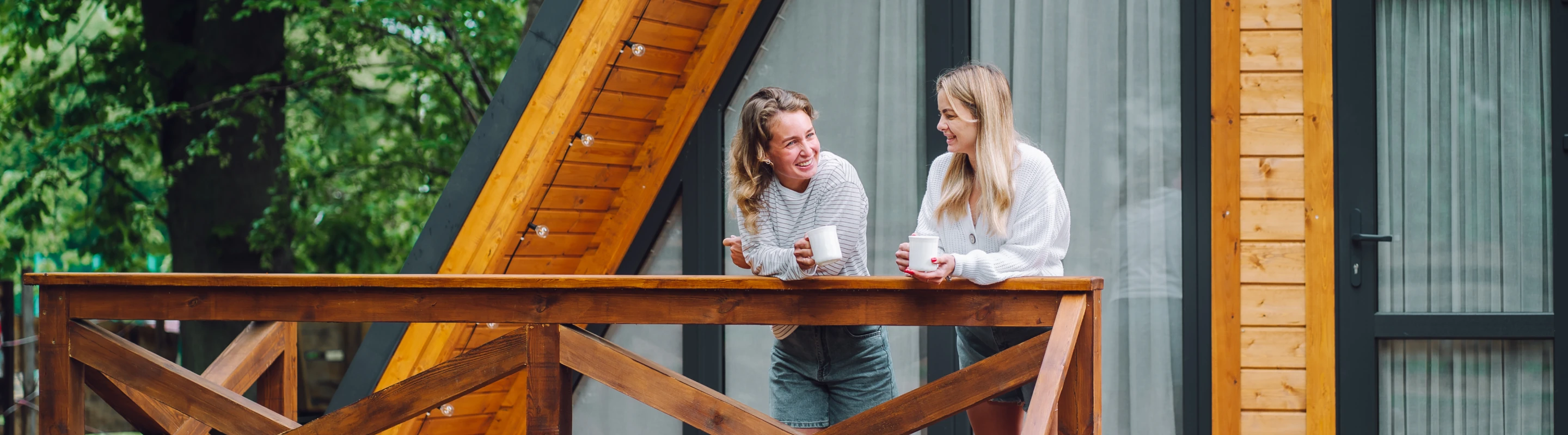 Two young women with vacation rental travel insurance having coffee on the front porch of a cabin
