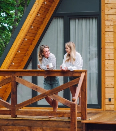 Two young women with vacation rental travel insurance having coffee on the front porch of a cabin