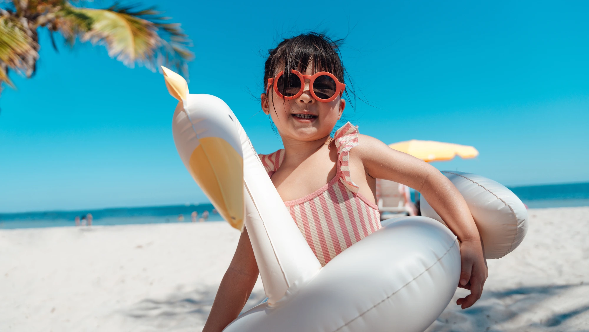 a child wears a swan floatie at the beach with coverage, after her parents researched "Is travel insurance worth it?"