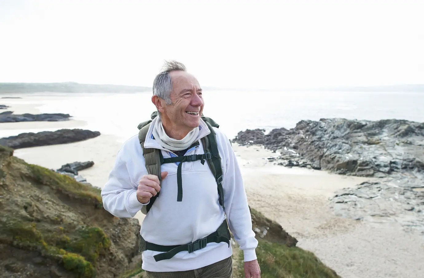 an older man with emergency medical travel insurance hikes along a rocky path by the ocean wearing light hiking gear