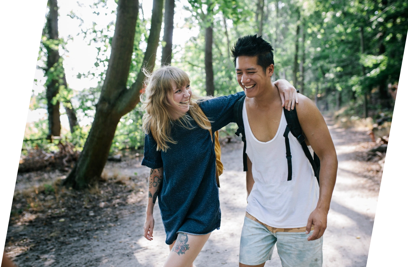 a young couple with travel insurance with primary coverage walk along a green trail through a forest with tall trees