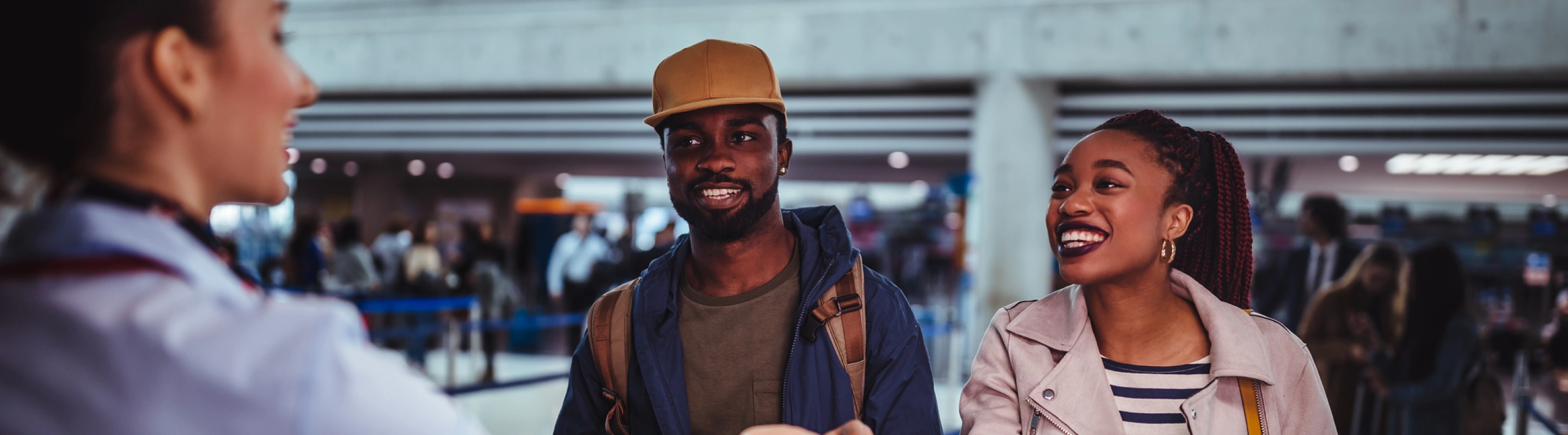 a young, black couple with couples' travel insurance speaks with an agent and hands over their boarding passes at the airport 