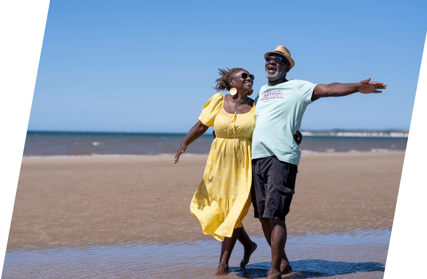 a black couple with travel insurance for trip cancellations embraces and smiles as they walk on a beach by the ocean