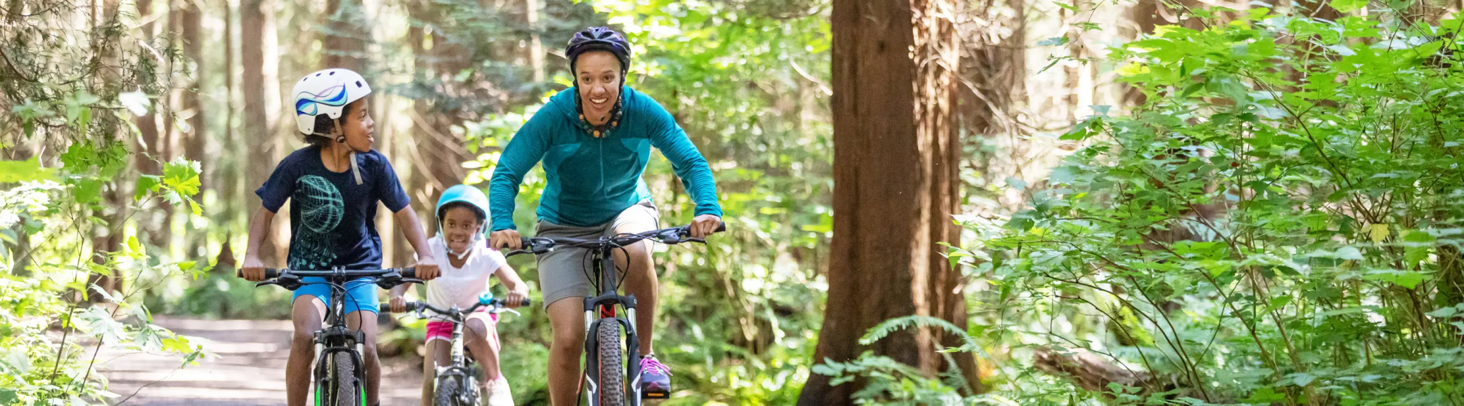 a mother and her two kids bike through a forest trail, enjoying an outdoor adventure with travel assistance available