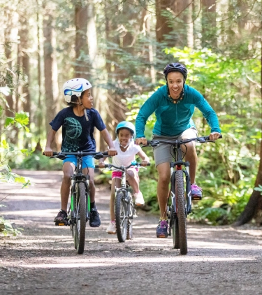 a mother and her two kids bike through a forest trail, enjoying an outdoor adventure with travel assistance available
