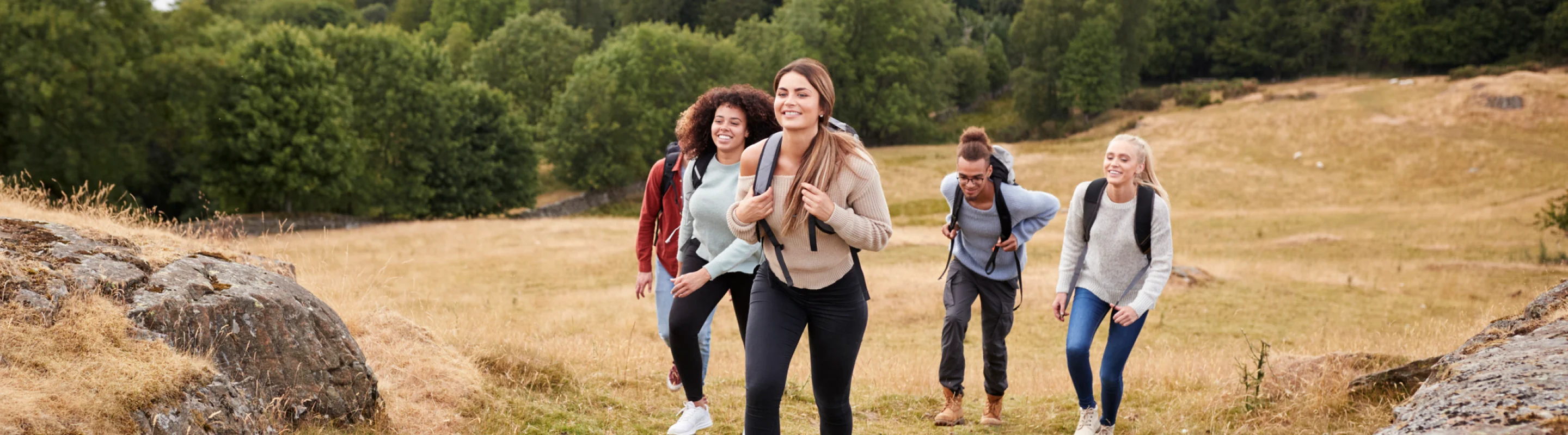a group of five young adults with travel insurance for students hikes through an open field wearing backpacks