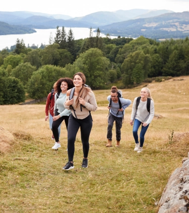 a group of five young adults with travel insurance for students hikes through an open field wearing backpacks