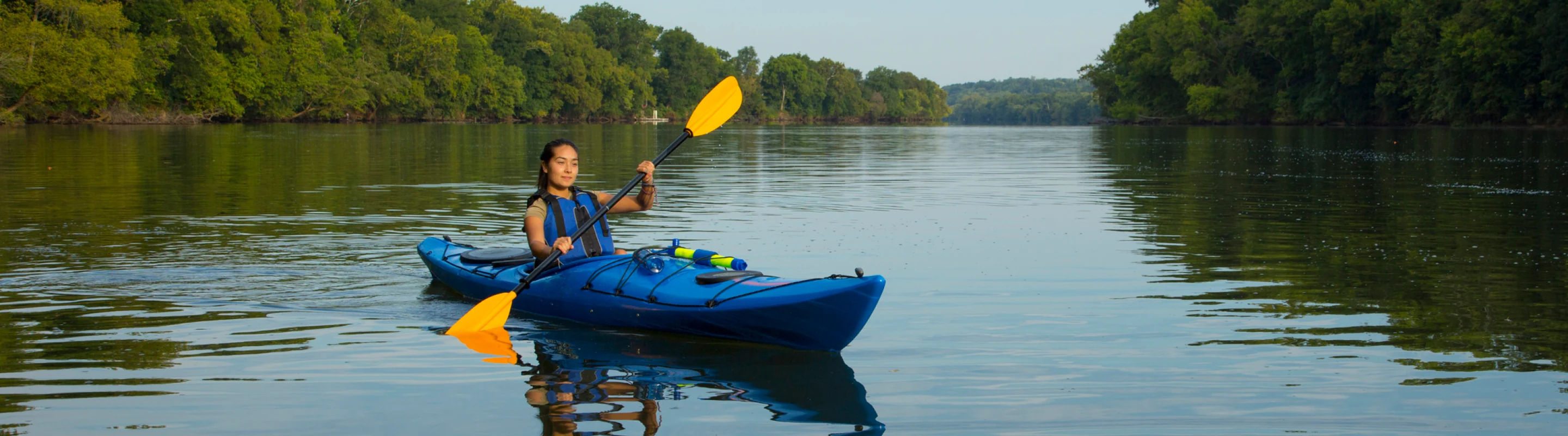 a young female with travel insurance for medical evacuations kayaks with yellow paddles on a calm river