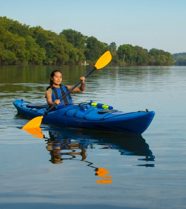 a young female with travel insurance for medical evacuations kayaks with yellow paddles on a calm river