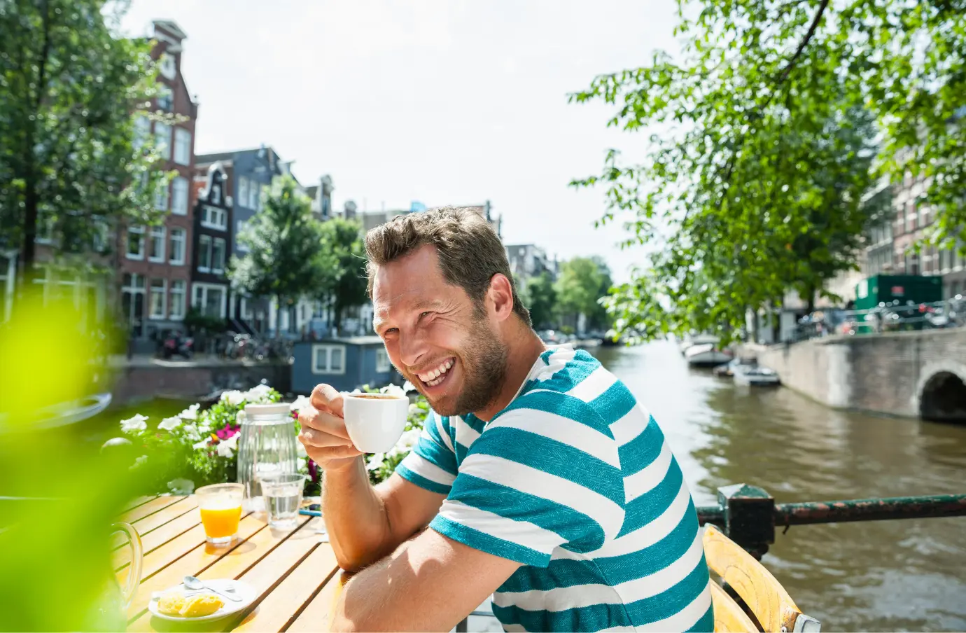a middle-aged man enjoys breakfast on a canal in Amsterdam on vacation after learning about Travelex insurance 