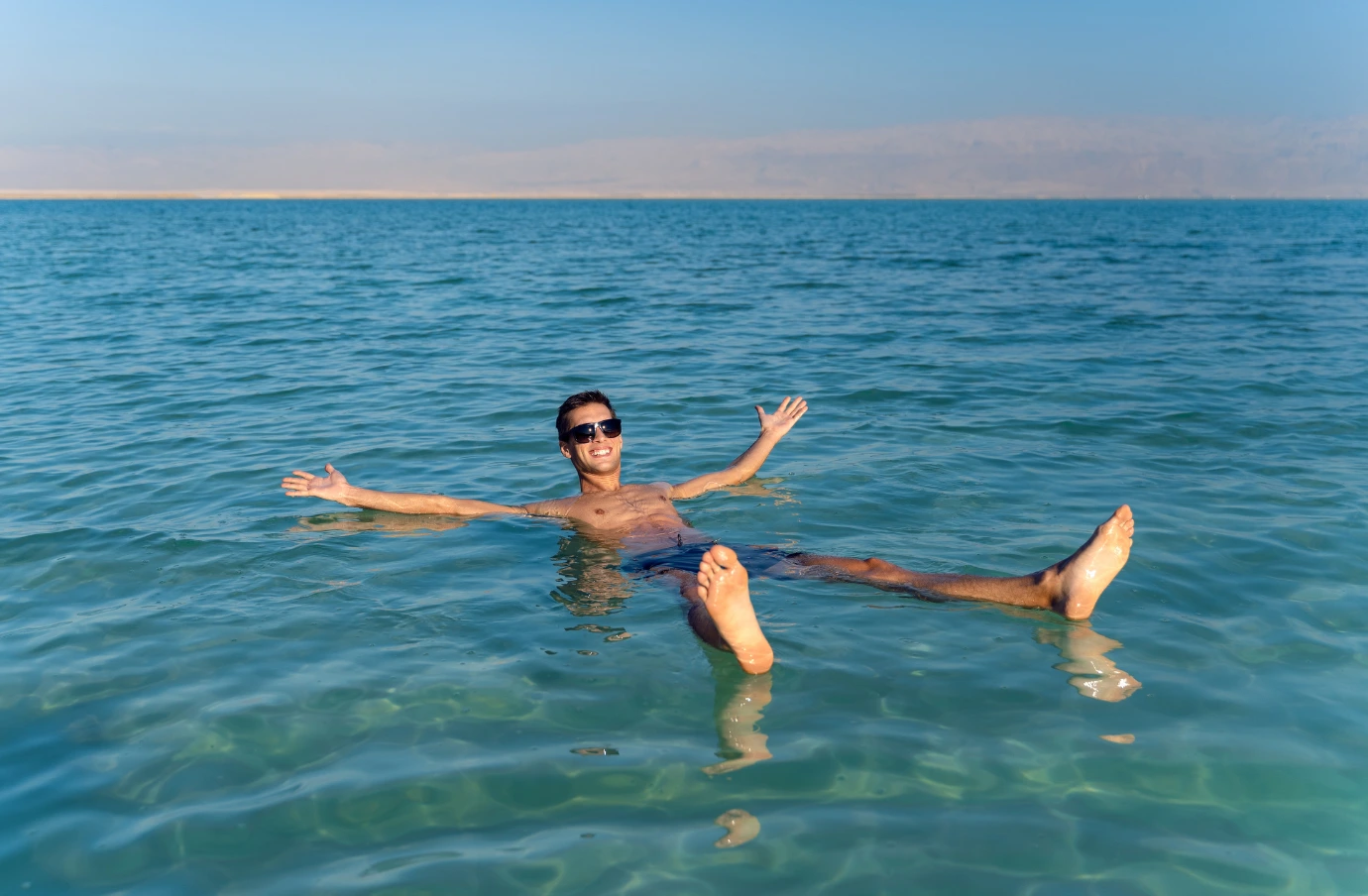 a young man wearing sunglasses smiles as he floats in the Dead Sea, insured with travel insurance for Israel 