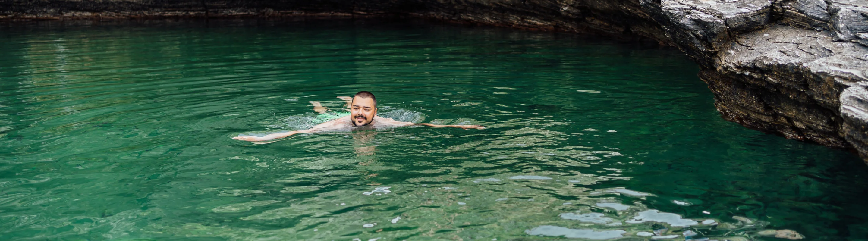 a young man with travel insurance with primary coverage swims in a natural, turquoise lagoon near rocks