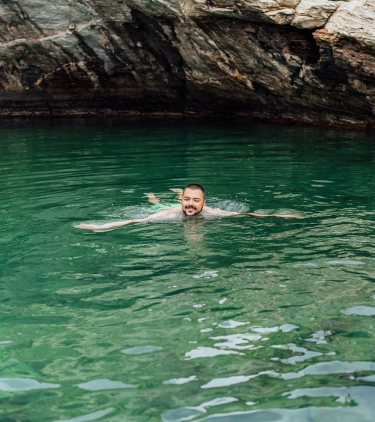 a young man with travel insurance with primary coverage swims in a natural, turquoise lagoon near rocks