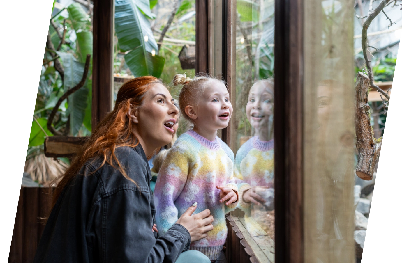 a mother with travel insurance for missed connections looks through a window with her toddler daughter at green plants 
