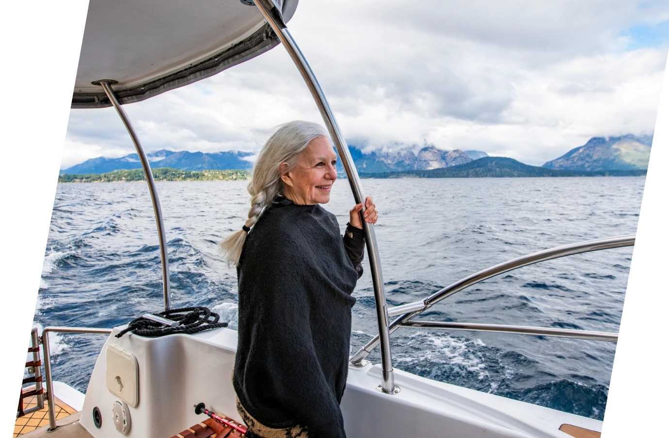 an older woman with travel insurance for medical evacuations stands on a boat and holds its railing on a cloudy day