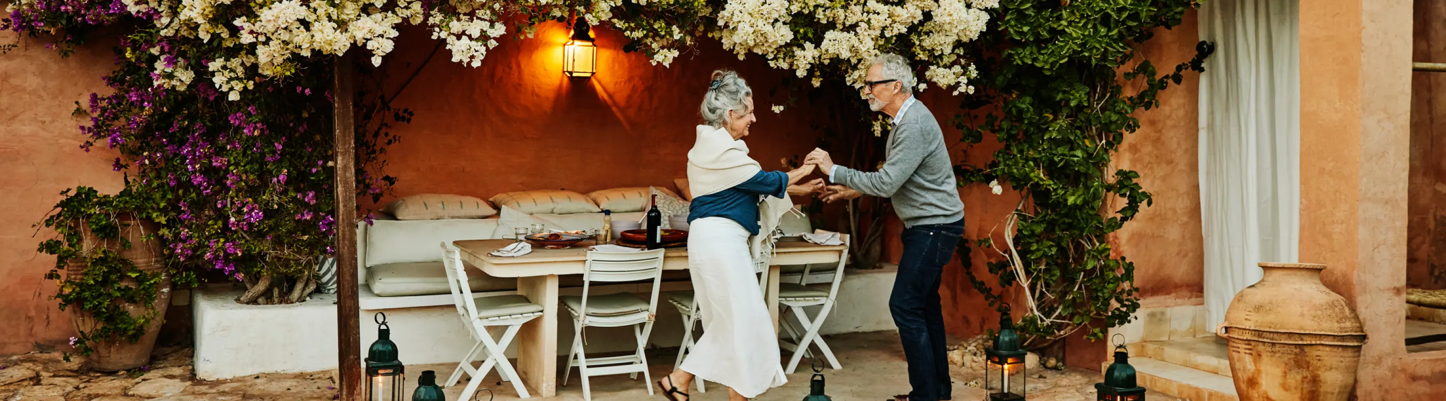 a senior couple with travel delay insurance dances on an outdoor patio in the Mediterranean under flowering vines