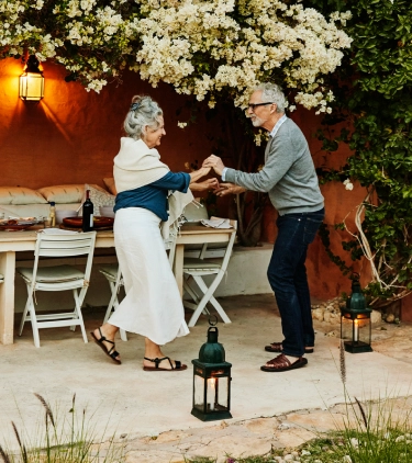 a senior couple with travel delay insurance dances on an outdoor patio in the Mediterranean under flowering vines