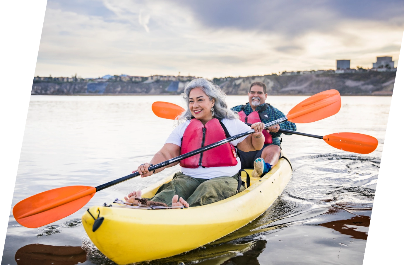a senior couple with travel delay insurance kayaks on calm water with paddles in a yellow boat on a cloudy day