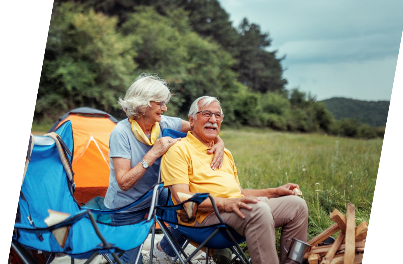a senior couple with travel delay insurance sits on foldable chairs by a campfire in their campsite on a sunny day