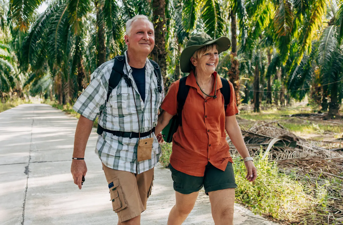 an older couple with backpacks hikes along a palm grove path on vacation after learning about Travelex travel insurance 