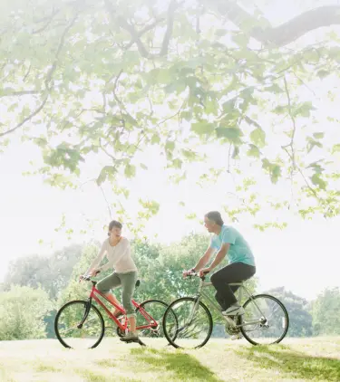a man and woman cycle through a green park on vacation after learning about Travelex insurance 