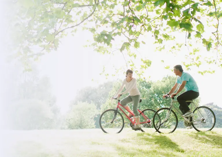 a man and woman cycle through a green park on vacation after learning about Travelex insurance 