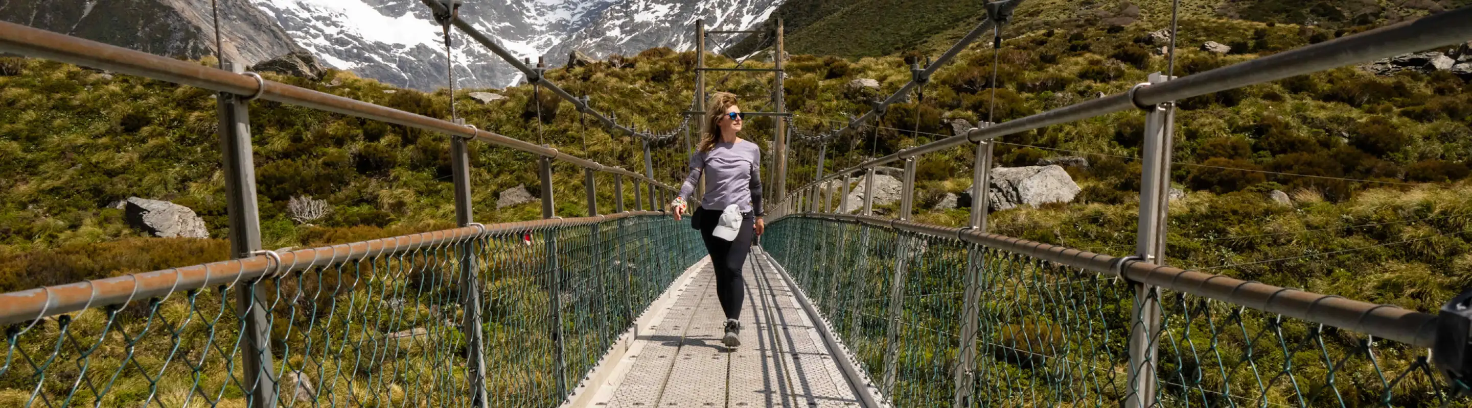 a young woman with travel insurance for pre-existing conditions crosses a suspension bridge in the mountains 