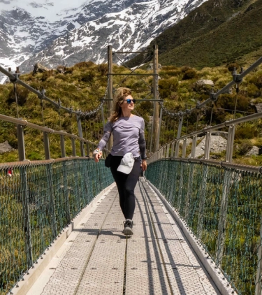 a young woman with travel insurance for pre-existing conditions crosses a suspension bridge in the mountains 