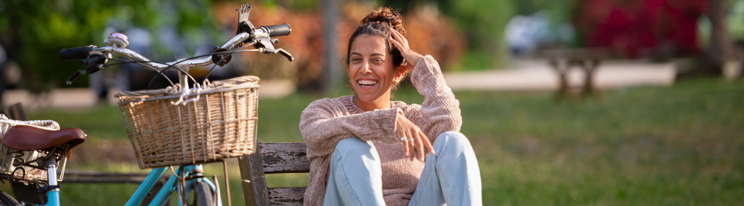 a young woman with travel insurance for Israel relaxes on a park bench next to a blue bicycle 