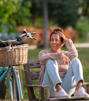 a young woman with travel insurance for Israel relaxes on a park bench next to a blue bicycle 