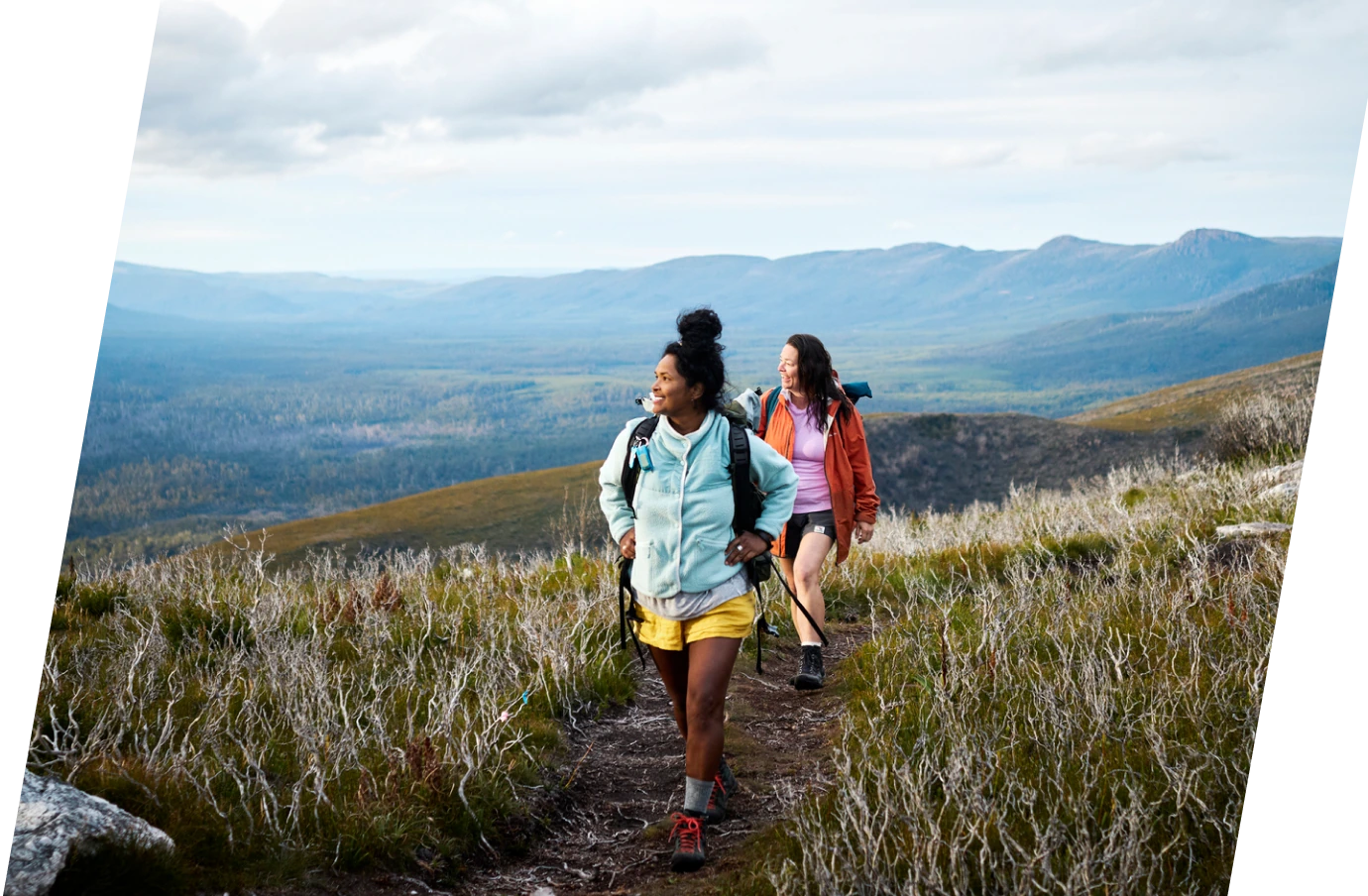 two young women with travel insurance for missed connections hike on a grassy mountain trail