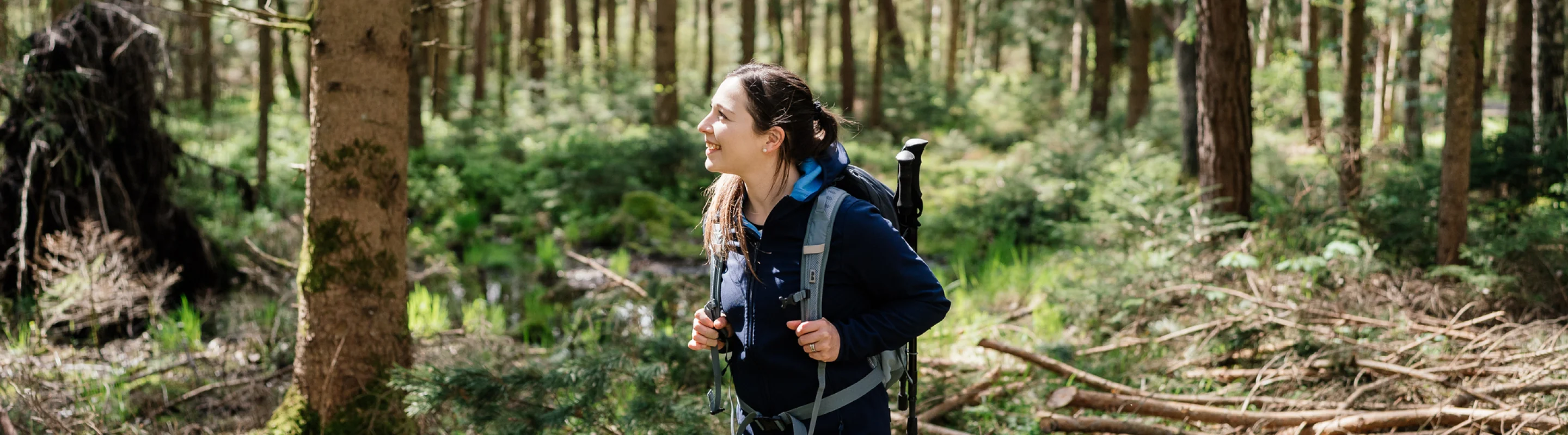 a young, brunette woman with travel insurance for students hikes through a forest wearing a backpack
