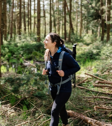 a young, brunette woman with travel insurance for students hikes through a forest wearing a backpack