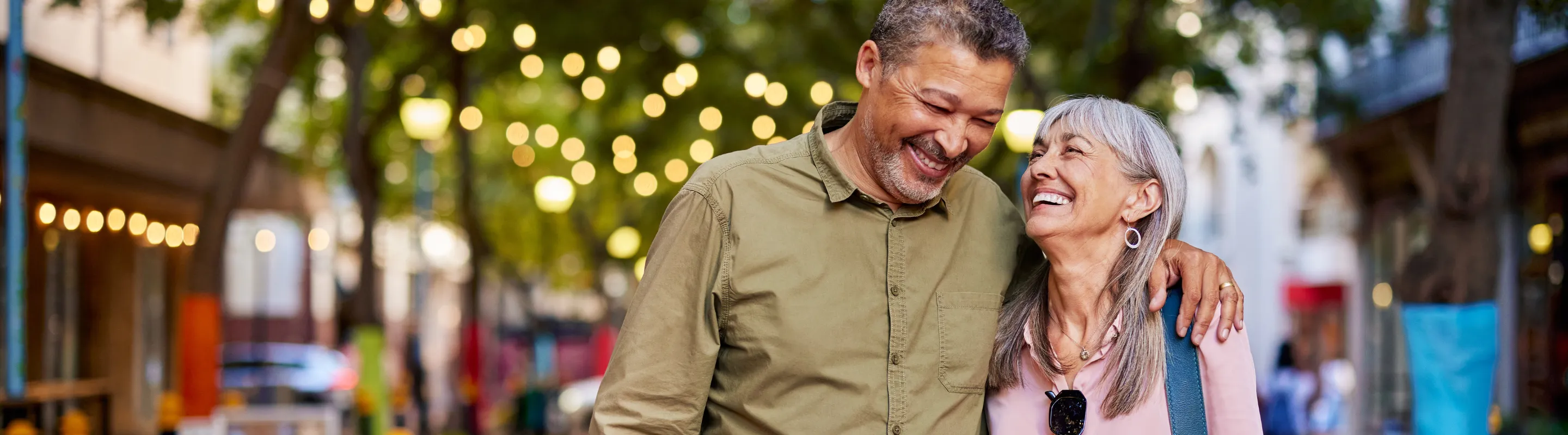 an older couple embraces as they walk through a quaint neighborhood, insured with travel insurance for city trips
