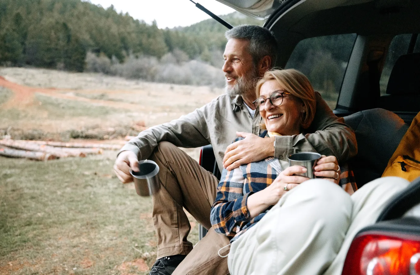 an older couple drinks coffee from the trunk of their SUV in the morning, insured with road trip travel insurance 