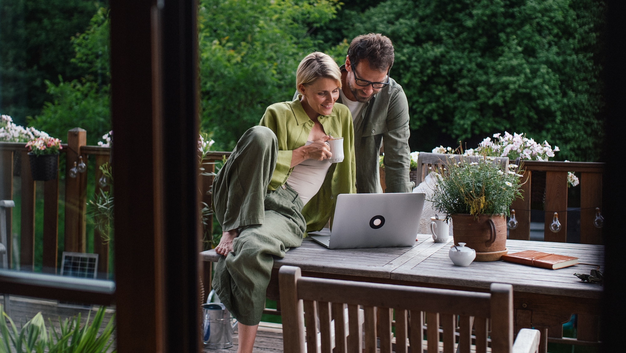 a couple looks at a laptop on their deck outdoors, researching "How much is travel insurance?"