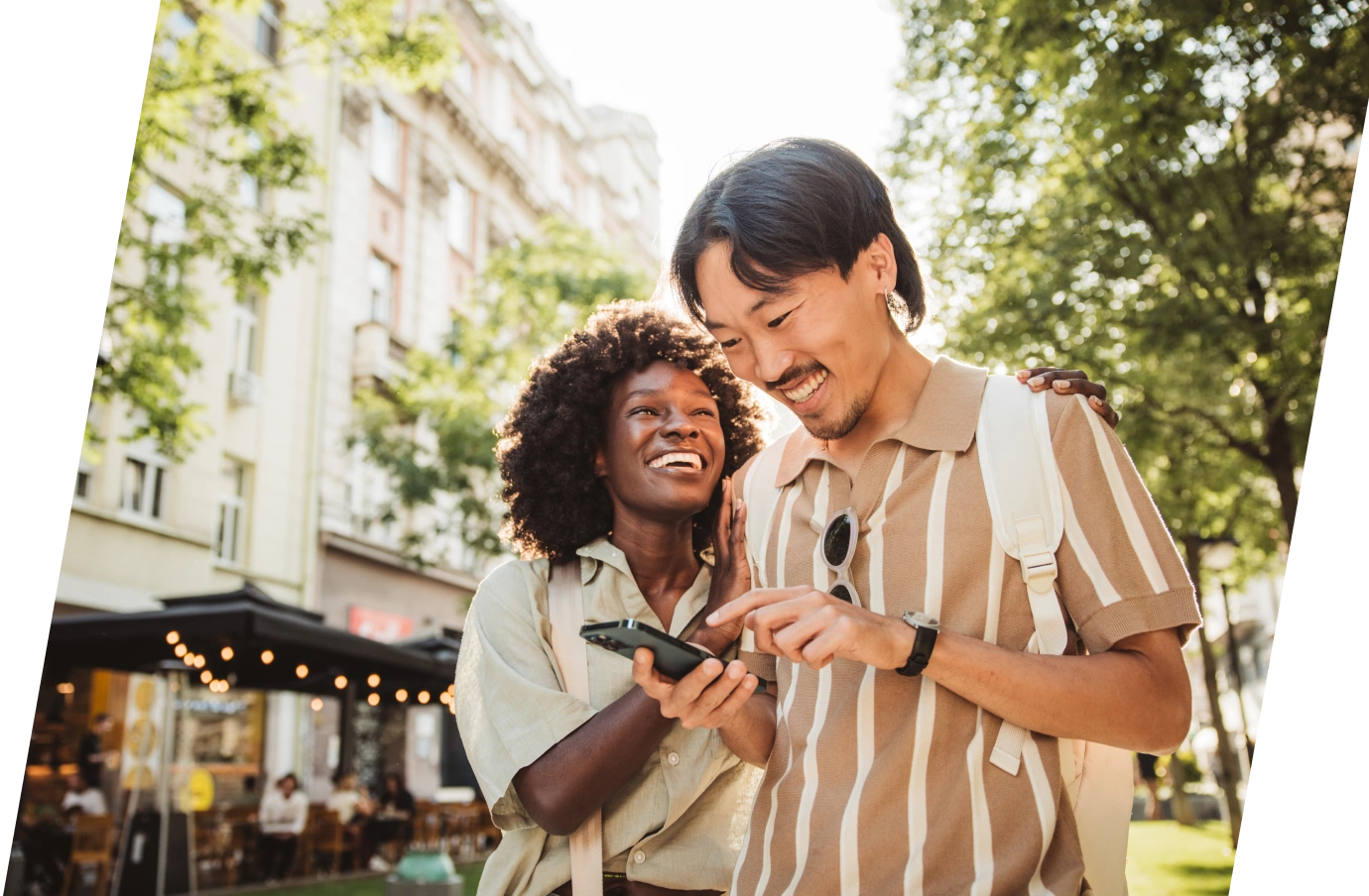 Young couple with travel insurance for digital nomads smiling and looking at a smartphone while walking on the street